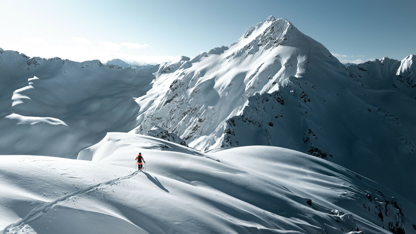 Een skiër op een besneeuwd berglandschap onder fel zonlicht, omringd door majestueuze toppen en ongerepte sneeuw.